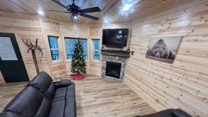 L’intérieur d’un chalet accueillant, avec une cheminée, un sapin de Noël, un téléviseur et un canapé en cuir.