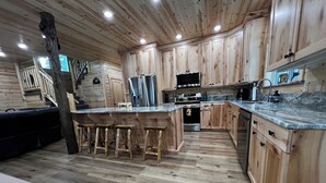 Une cuisine moderne avec des meubles en bois, un îlot central doté de tabourets, des appareils en acier inoxydable et un plan de travail en marbre.