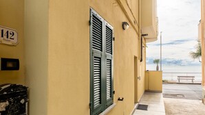 Ein gelbes Gebäude mit Fenster, Rollläden und einem Schild mit der Aufschrift '142', sowie eine Bank am Wasser.