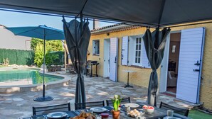 Un área de comedor al aire libre con una mesa lista para comer, una piscina y un porche cubierto.