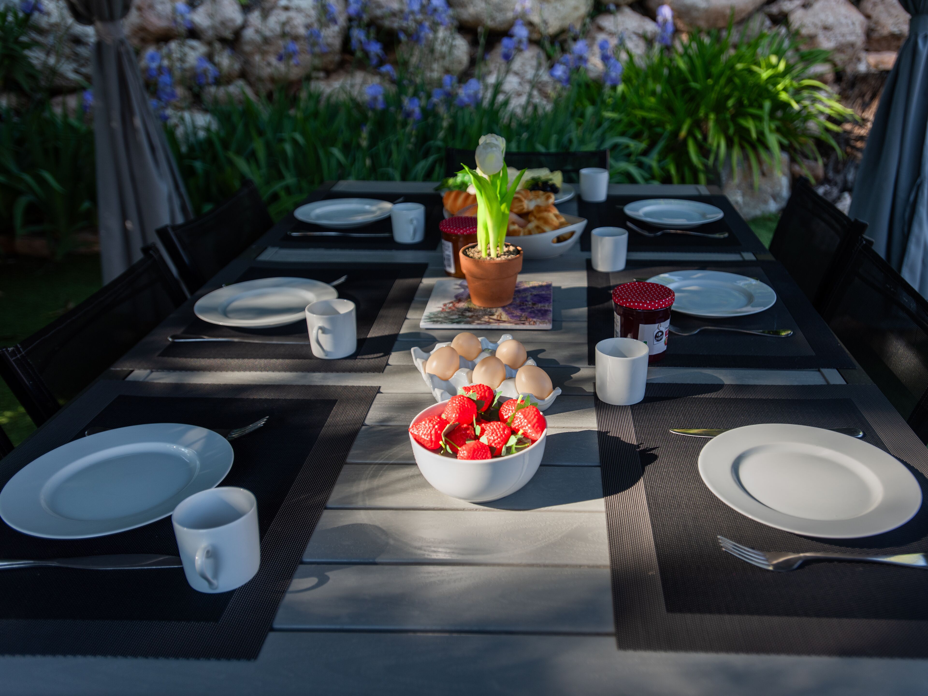 Een eettafel buiten gedekt met borden, bekers en een schaal aardbeien.