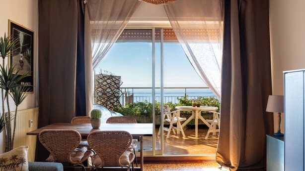 Une pièce comprenant un coin repas, un canapé et offrant une vue sur la mer grâce à de grandes fenêtres.