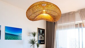 Une pièce avec un luminaire suspendu en fibres tressées, des tableaux encadrés accrochés au mur et une fenêtre avec des rideaux.
