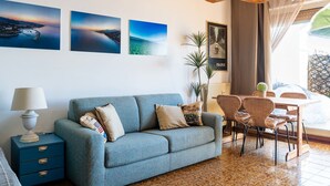 Un salon moderne avec un canapé bleu, une table à manger entourée de chaises en osier et un grand luminaire tressé.