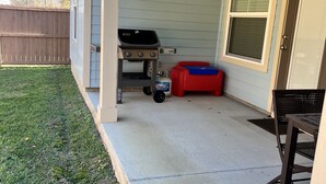 Ein überdachter Patio-Bereich mit Grill, rotem Staufach und schwarzem Metallstuhl.