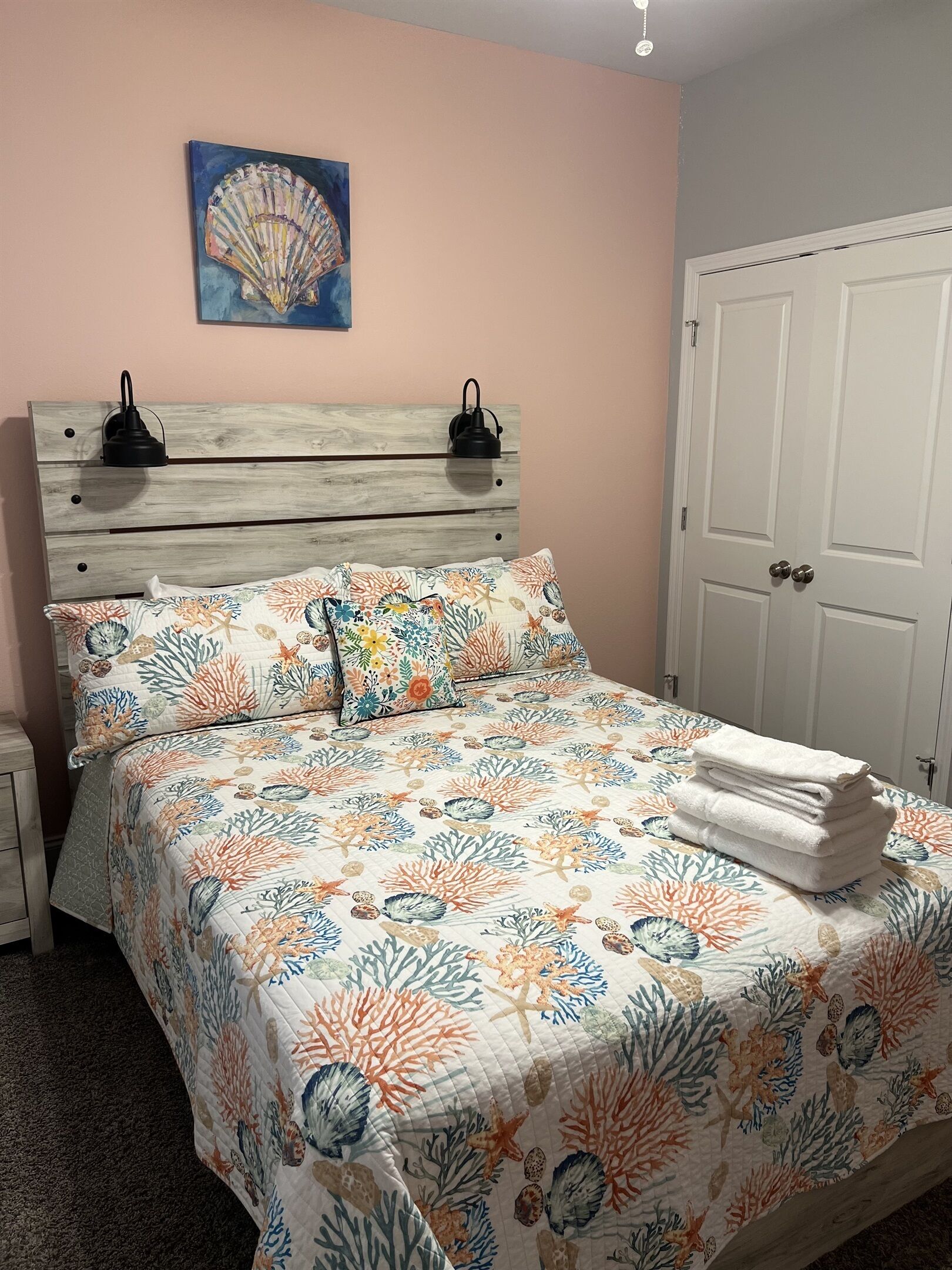 A bedroom with a bed, a nightstand, a wall-mounted lamp, and a door.
