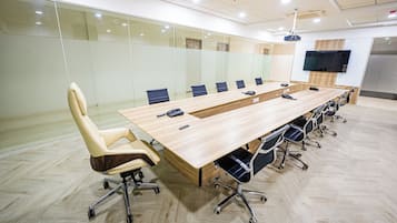 Uma sala de conferência com uma mesa comprida, várias cadeiras, um projetor e uma TV na parede.