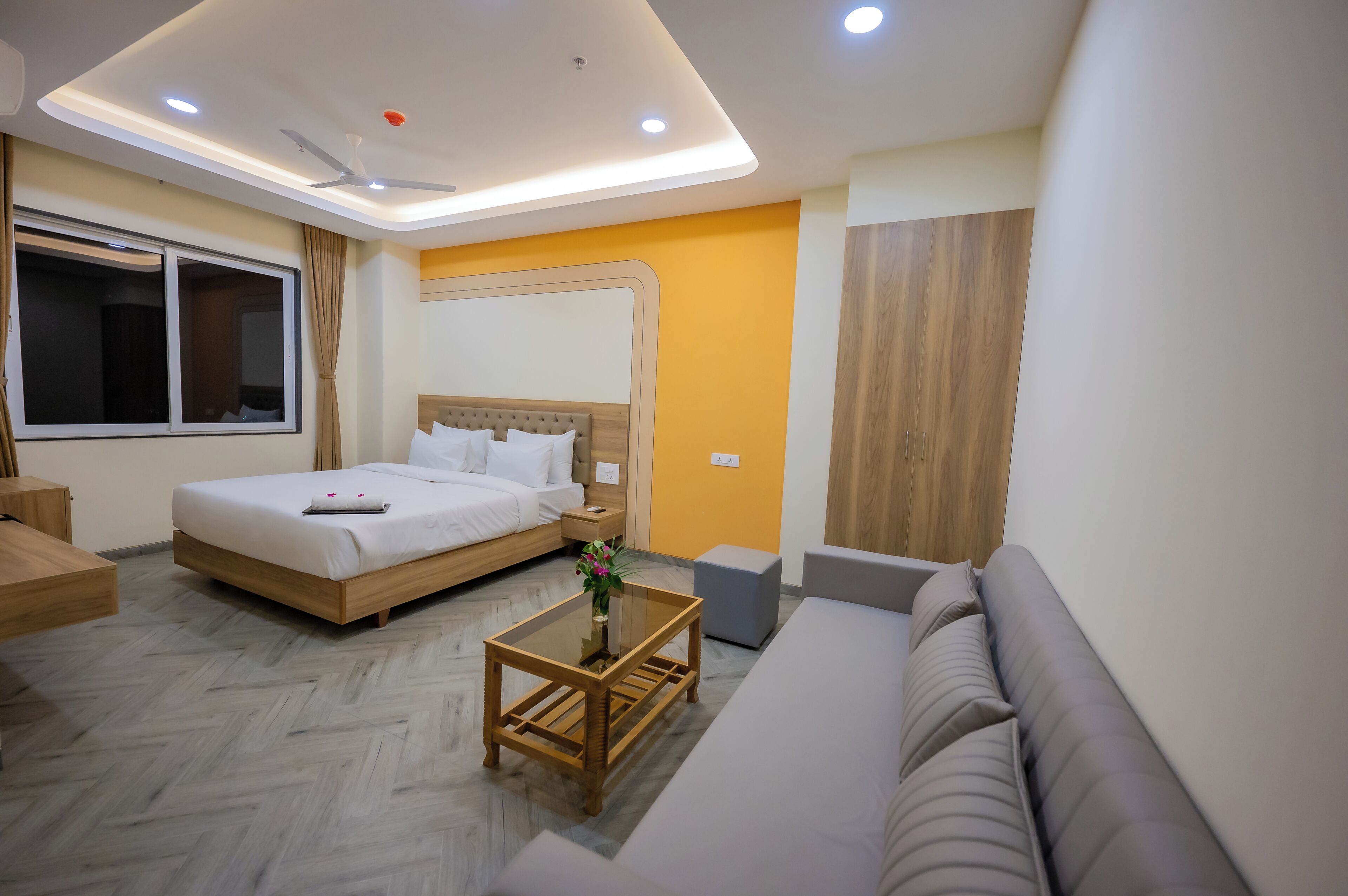 A modern hotel room with a bed, a sofa, a small table, and a window.