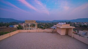 A rooftop terrace with a view of a town and hills. - Lotus Leaf (Sudhagad)