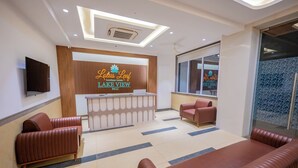 A hotel reception area with a wooden reception desk, leather seating, and a large window. - Lotus Leaf (Sudhagad)