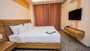A hotel room with a bed, bedside tables, a flat-screen TV, and a wooden bedside console.