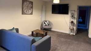 A living room with a blue sofa, a coffee table, a gray armchair, a TV, and a painting on the wall.