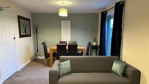 A living room with a sofa, a dining table with chairs, a floor lamp, and a window with curtains.