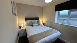A bedroom with a bed, bedside tables, a lamp, a window, and a radiator.