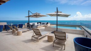 Un solàrium amb seients exteriors, ombrel·les i una piscina amb vista al mar.