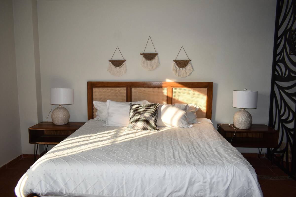 A neatly made bed with a white quilt and pillows, flanked by two bedside tables with lamps and decorative items.