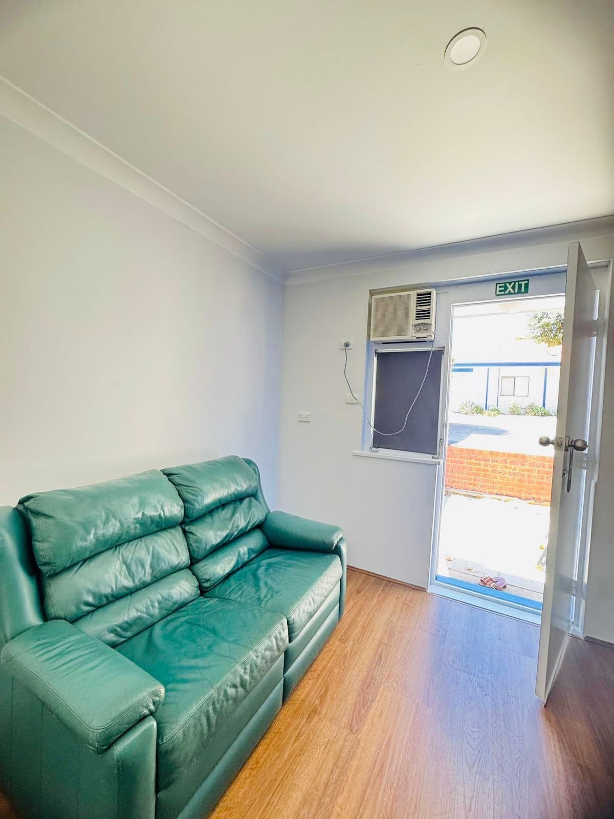 A room with a green leather sofa, an air conditioning unit, and an exit door.