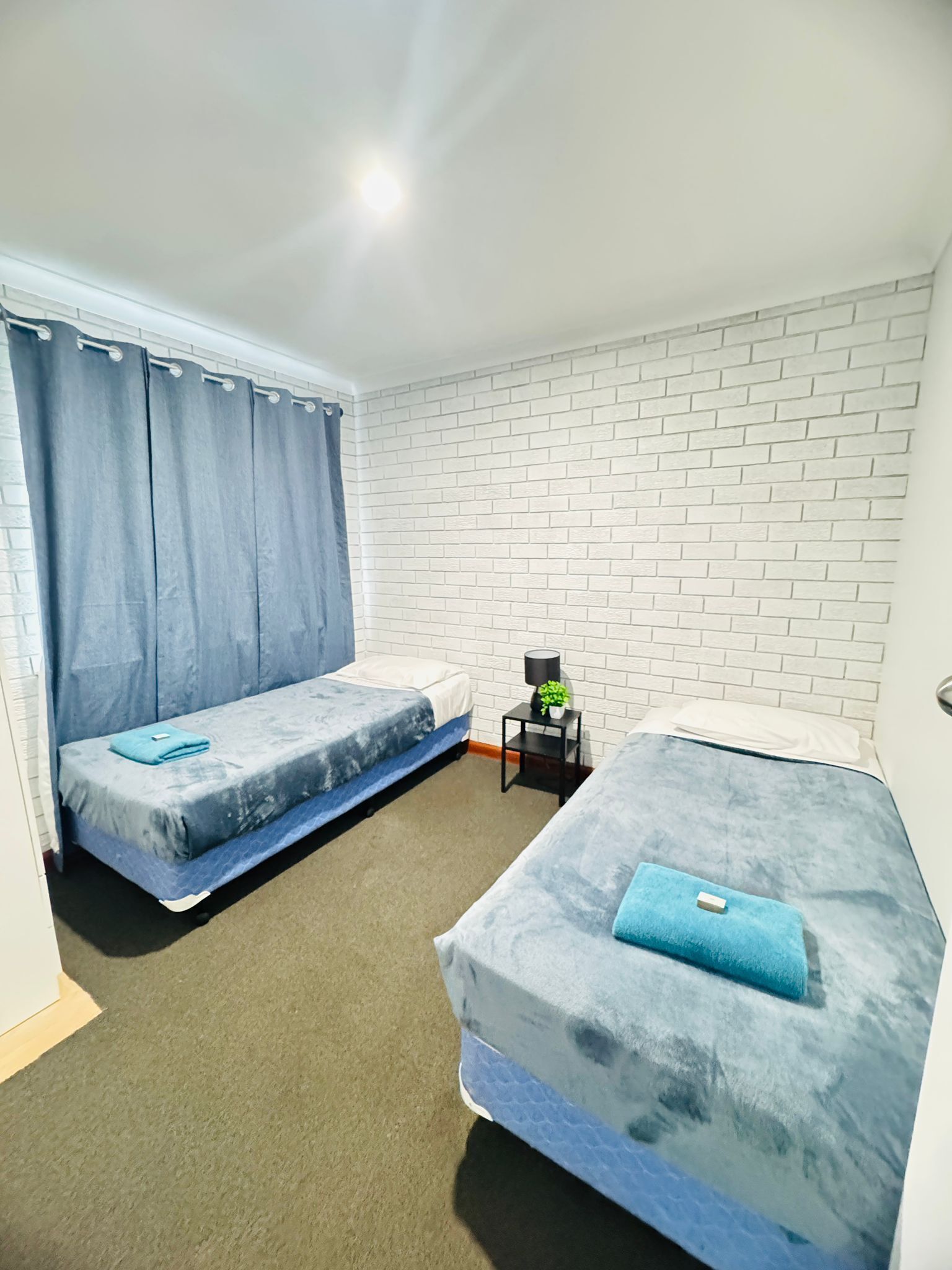 Een kamer met twee bedden, een kleine tafel met een plant en een witte bakstenen muur.