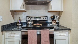 Una cocina con armarios blancos, estufa de acero inoxidable y salpicadero de azulejos.