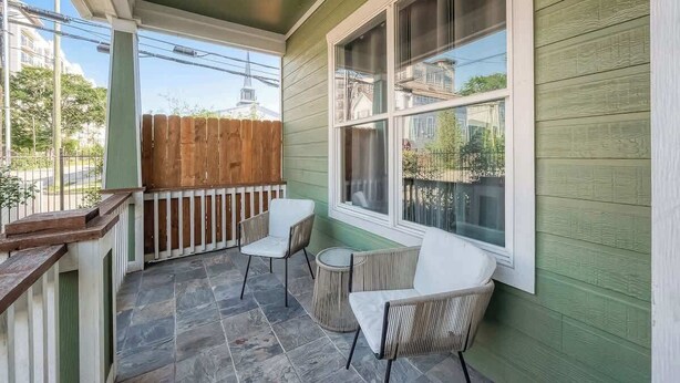 A covered porch with a wooden fence, two white chairs, a small round table, and a large window. - Cozy Modern Loft 1BR/1BA - Peace and comfort (Houston)