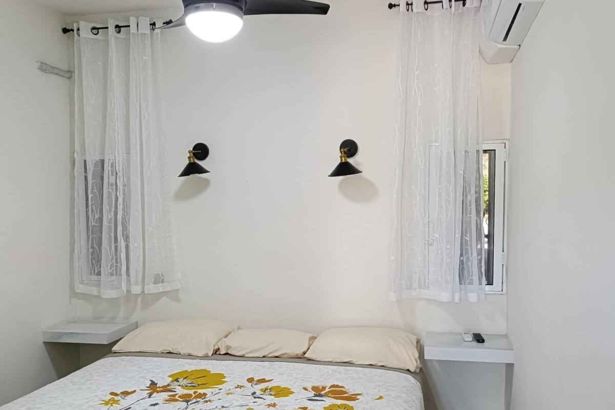 Een slaapkamer met een bed, twee nachtkastjes, een plafondventilator, twee wandlampen en een airconditioning.