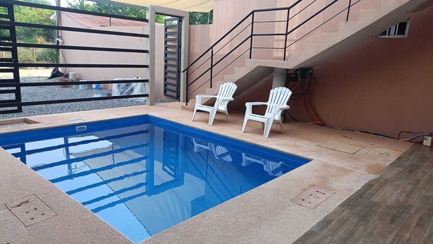 A swimming pool with two white chairs, a staircase, and a gated entrance.