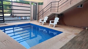 Une piscine avec deux chaises blanches, un escalier et une entrée fermée par un portail.