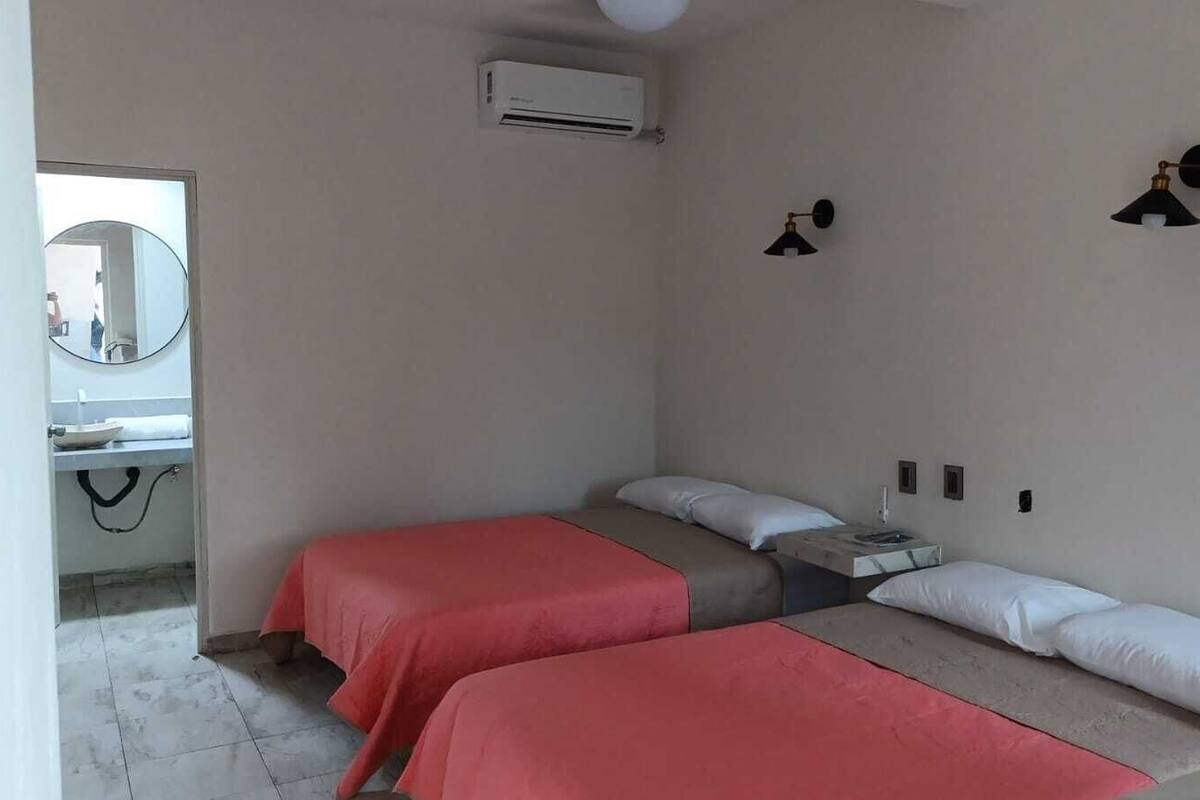 Een kamer met twee bedden, een klein tafeltje, een spiegel en een airconditioning.