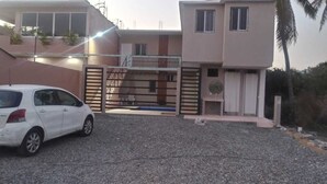 A multi-story building with a gated entrance, a car parked in front, and a palm tree in the background.