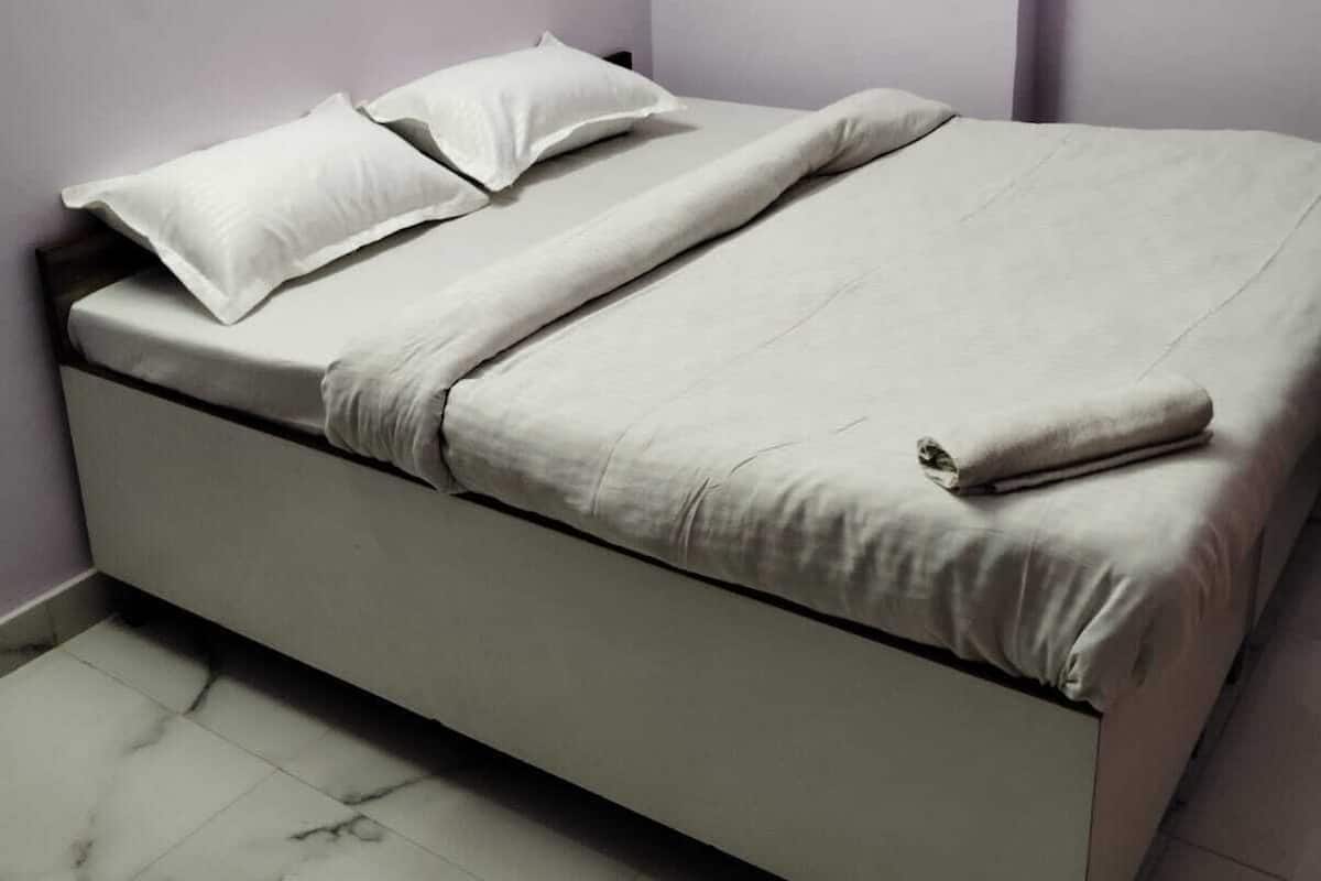 Una cama individual con colchón y almohadas en una habitación con suelo de mármol y paredes lisas.
