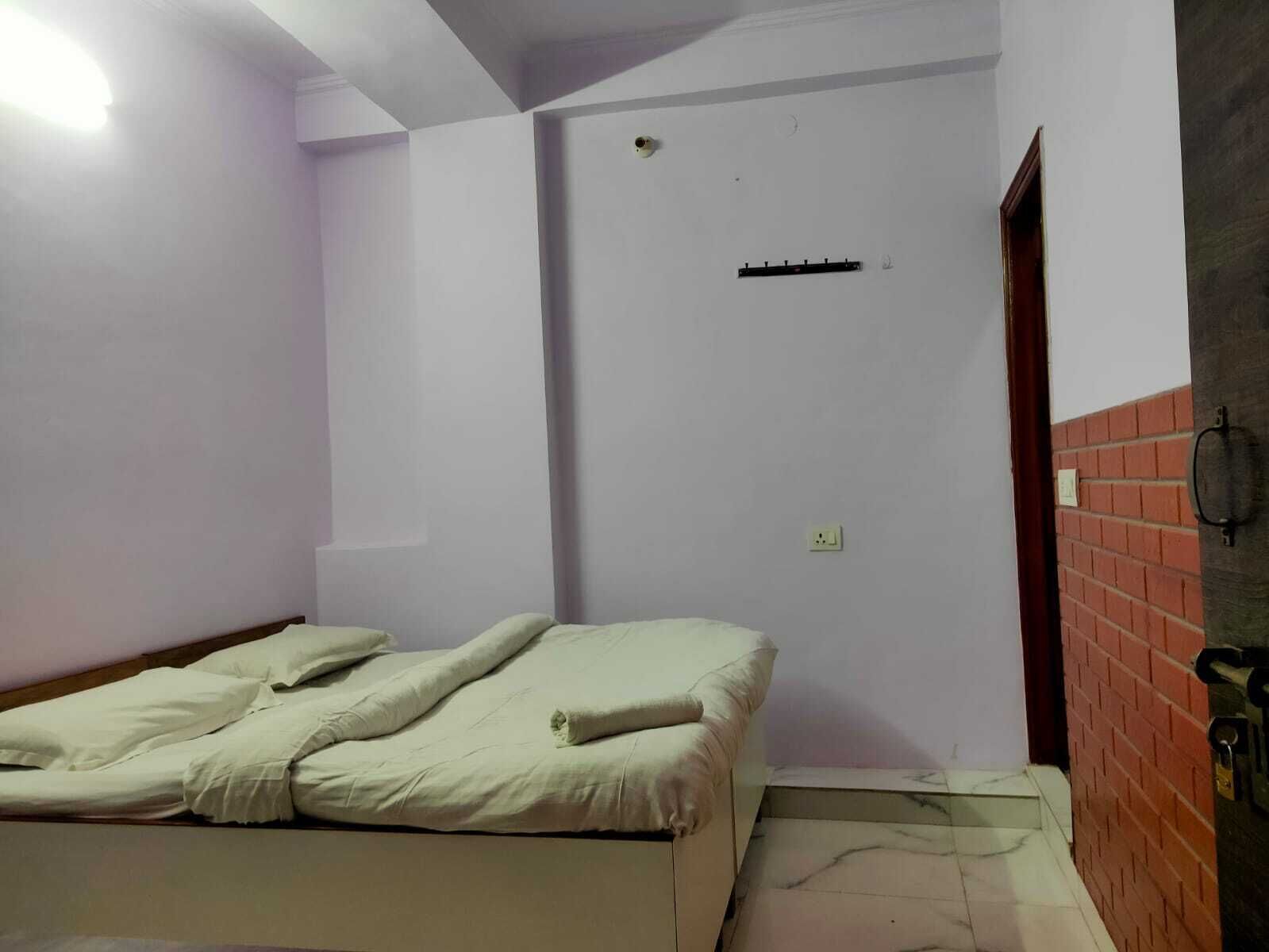 A small, sparsely furnished room with a single bed, a door, and a brick wall.