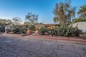Una casa de ladrillo rodeada de cactus y plantas desérticas, bajo un cielo despejado.
