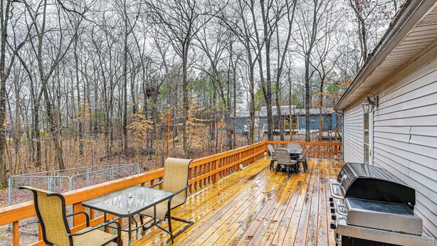 Eine Holzterrasse mit Gartenmöbeln, einem Grill und Blick auf ein bewaldetes Gebiet.