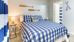 Ein Schlafzimmer mit kariertem Bettbezug, einem Nachttisch, einer Lampe und zwei Holzschlägern an der Wand.