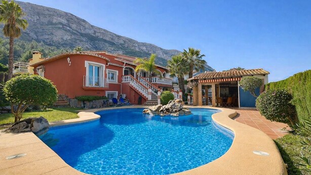 Une piscine avec une chaîne de montagnes en arrière-plan, un bâtiment rouge avec un escalier et un petit pavillon.