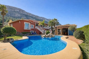 A swimming pool with a mountain backdrop, a red building with a staircase, and a small pavilion. - Serena Vista - Denia, Costa Blanca (Denia)