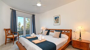 Une chambre avec un grand lit, une chaise en bois, une table de chevet et une vue par la fenêtre.