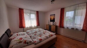 Ein Schlafzimmer mit Bett, Schminktisch, Nachttisch, einem Gemälde und einem Fenster mit Vorhängen.