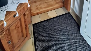 Käytävä, jossa on puinen ovikehys, ruukussa oleva kasvi, puinen lipasto, kuvioitu matto ja patteri.