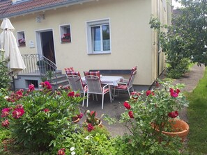 Eine Terrasse mit Tisch und Stühlen, einem Sonnenschirm und Kübelpflanzen mit Blumen.
