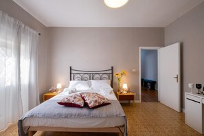 Une chambre à coucher comprenant un lit, des tables de chevet, une commode, une lampe, un vase avec des fleurs et une porte donnant sur une autre pièce.