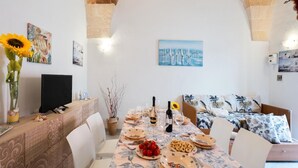 Un comedor con una mesa dispuesta para cuatro personas, un sofá y un televisor sobre un mueble.
