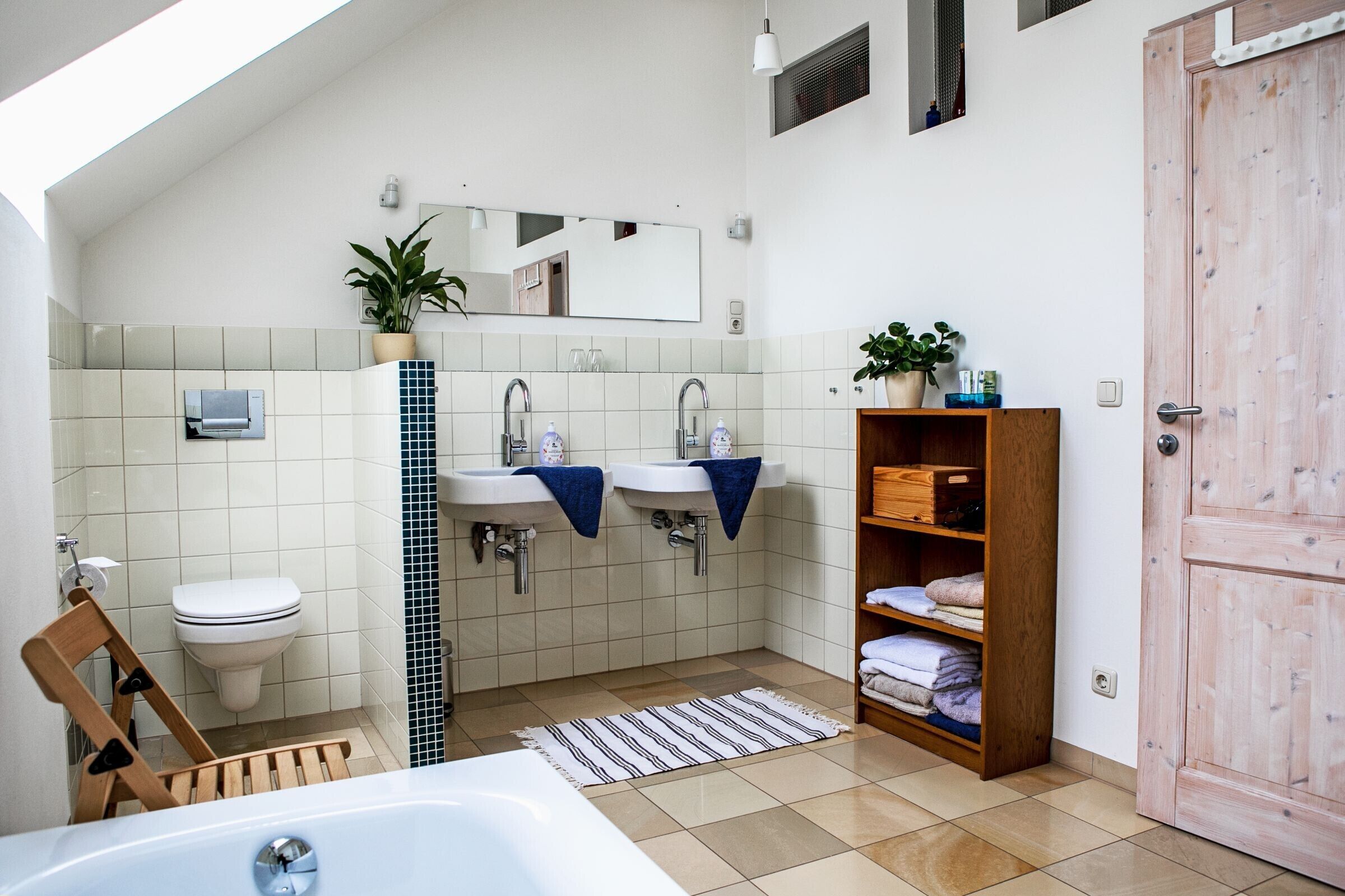 Ein Badezimmer mit einer Badewanne, zwei Waschbecken, einer Toilette, einer hölzernen Ablage mit Handtüchern und einem Spiegel.