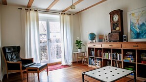 A room with a wooden floor, a black leather chair, a small table, a bookshelf, a globe, and a clock.