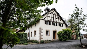 A traditional half-timbered house with a steep gabled roof, a stone foundation, and a gravel driveway.