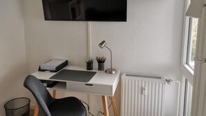 Un bureau blanc avec un téléviseur à écran plat, une lampe et un ordinateur.