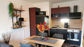 Une cuisine compacte dotée d’appareils électroménagers modernes, un coin repas avec une table et des chaises, et un petit espace de vie comprenant un canapé et des objets de décoration.