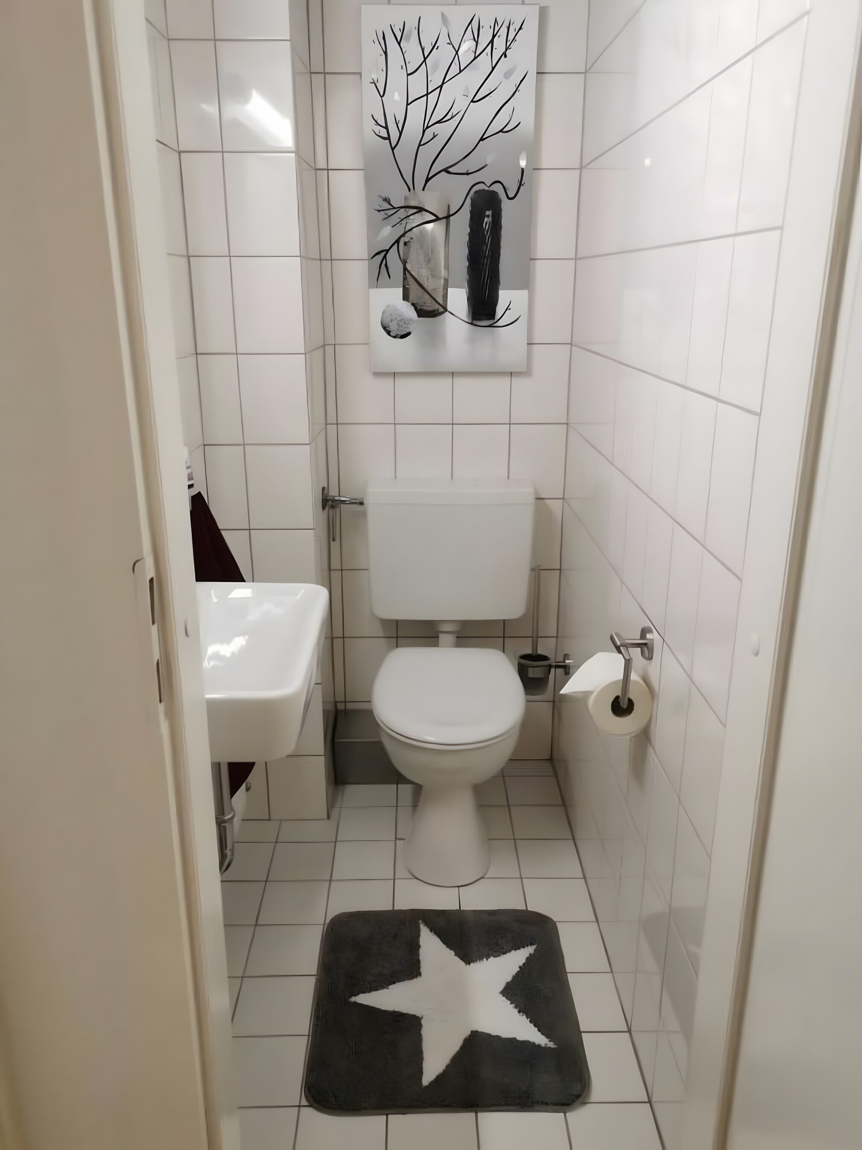 A small bathroom with a toilet, sink, and a decorative wall piece above the toilet.
