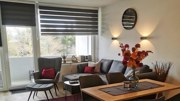 Un salon moderne comprenant un canapé, une table à manger, des chaises et une grande fenêtre avec des stores.