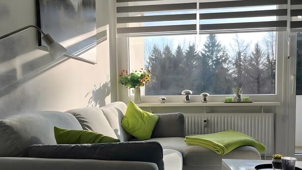 Un salon moderne avec un canapé, une table basse et une fenêtre équipée de stores.